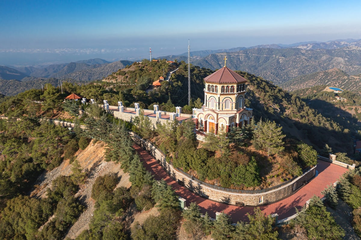 Aerial view of a monastery perched atop a hill with majestic mountains stretching in the background