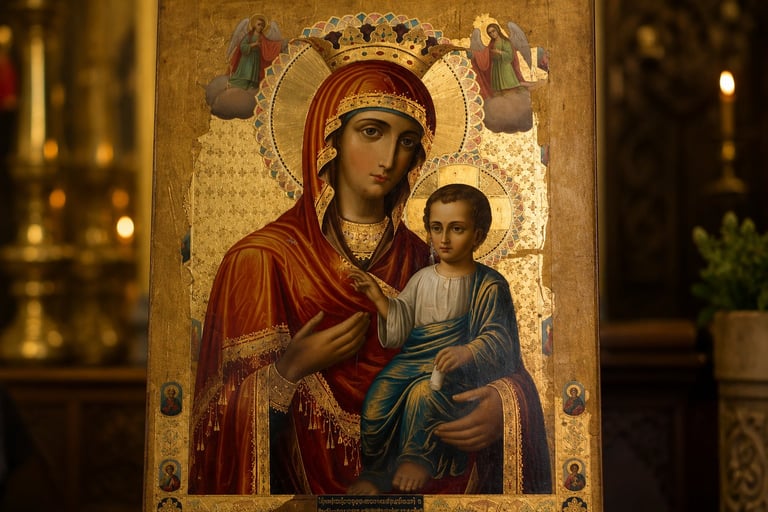Orthodox Christian icon depicting Virgin Mary in red robes holding Christ Child, with gold leaf background and ornate crown, lit by candles