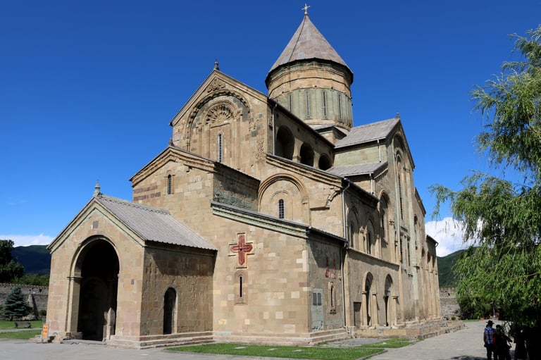 Ancient stone church with conical domed tower and arched entrance under blue sky