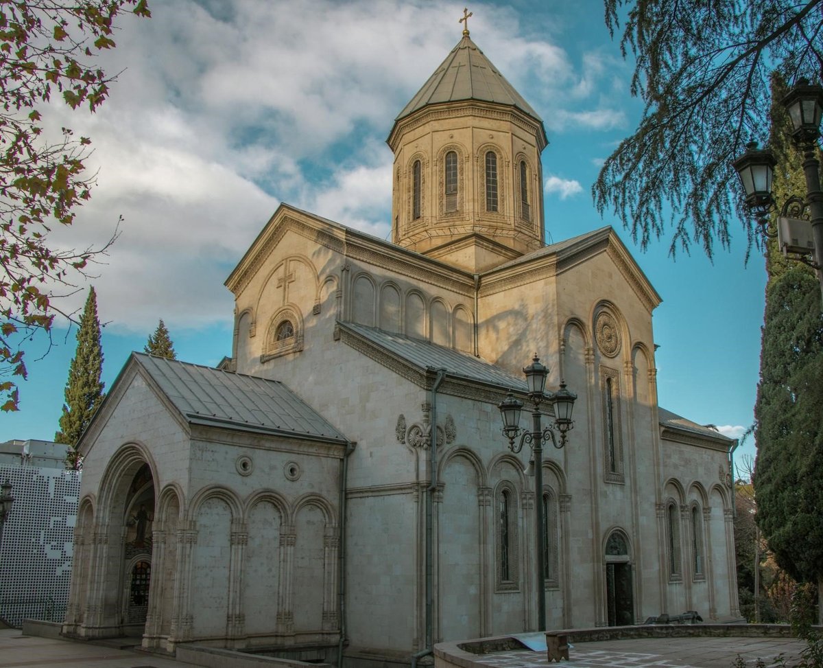 Eastern Orthodox church with golden dome, stone exterior, and cross on top against blue sky with clouds