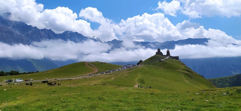 Green mountain meadow with a small church on a hilltop, snow-capped mountains and blue sky in background