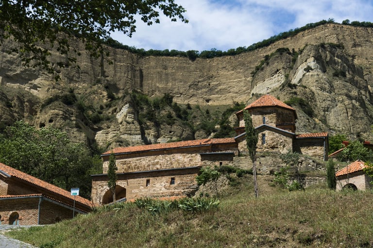 Ancient stone monastery with terracotta roofs built into a rocky hillside surrounded by lush green vegetation